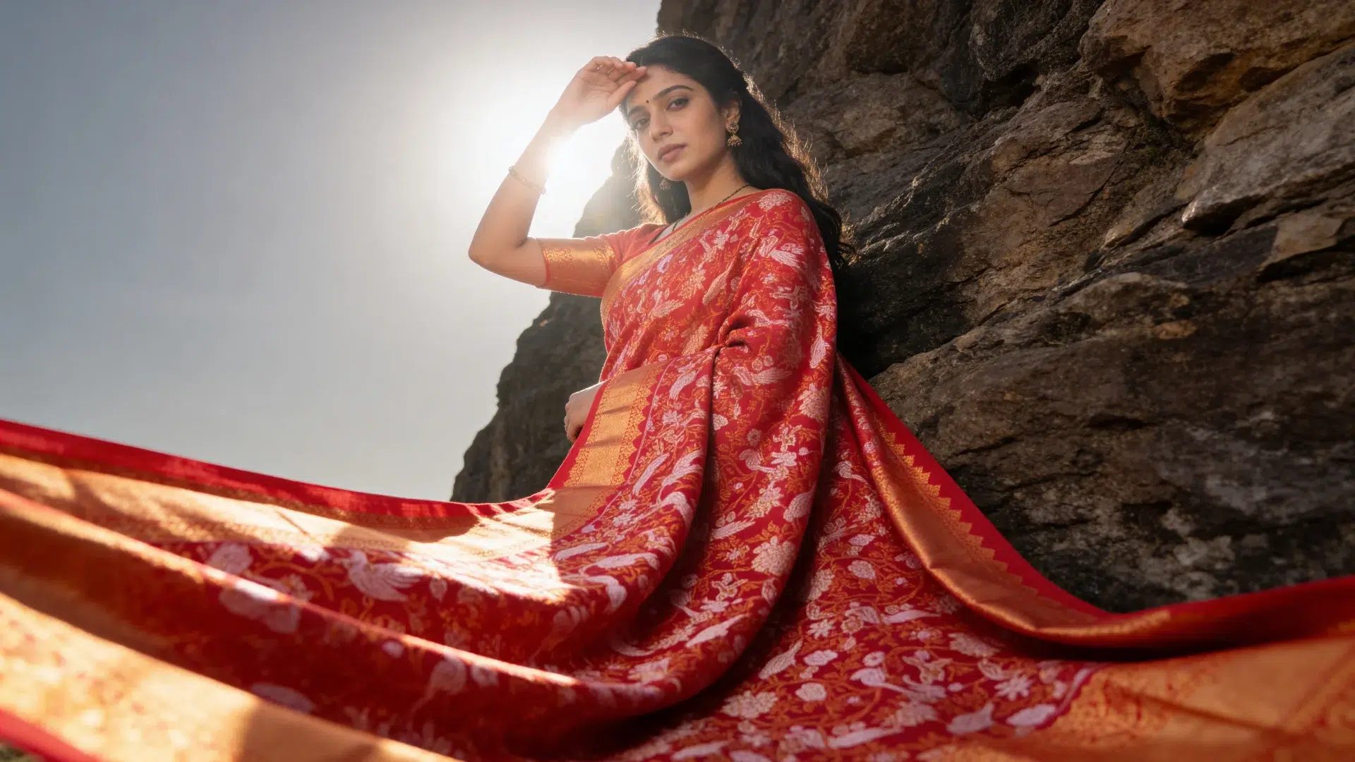 AI model by AIM Kreations in a red and gold silk saree posing against a rocky backdrop.